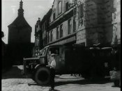 Automobil vyjíždí z domu v horní části náměstí č.p. 17. Ve sklepních prostorách - Muzeum strašidel. Vzadu je Poděbradova ulice s Rynáreckou bránou.